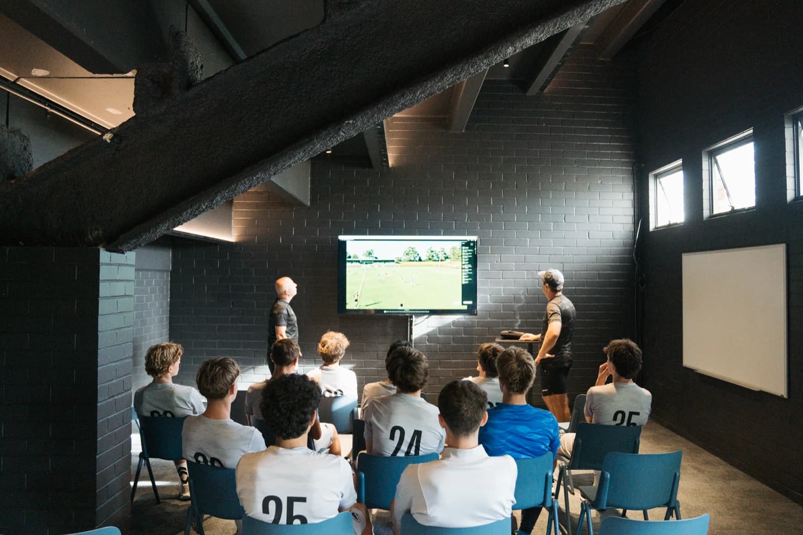 Sharks youth players in their white match shirts watching a coach break down match footage on the screen in the club’s video analysis room