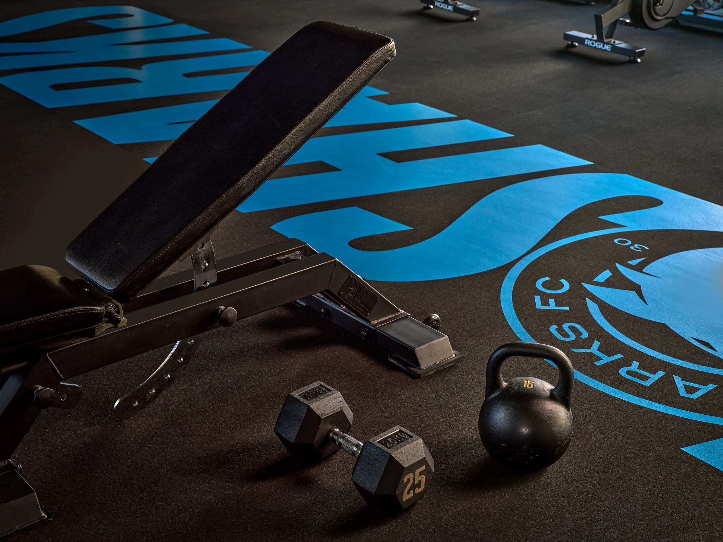A weights bench, a dumbbell and a kettlebell in the gym, the Sharks crest and “Sharks” painted in sky blue across the floor