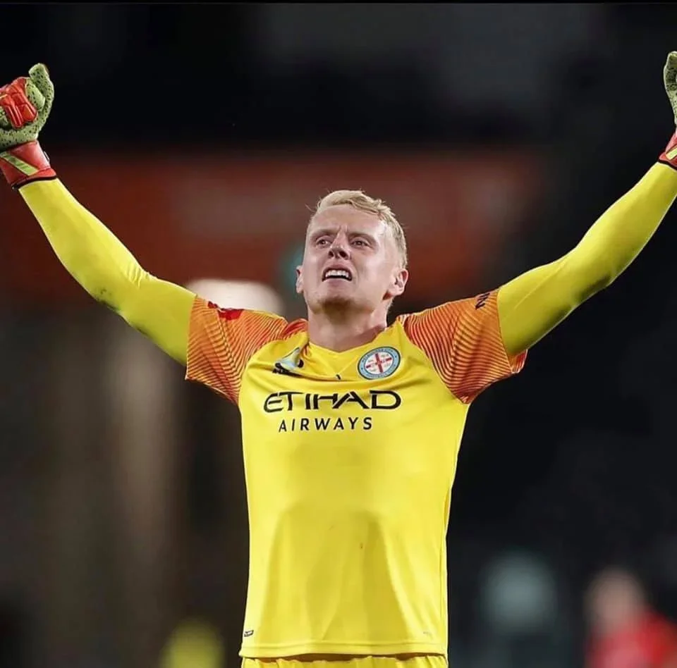 A goalkeeper in yellow celebrates with arms raised