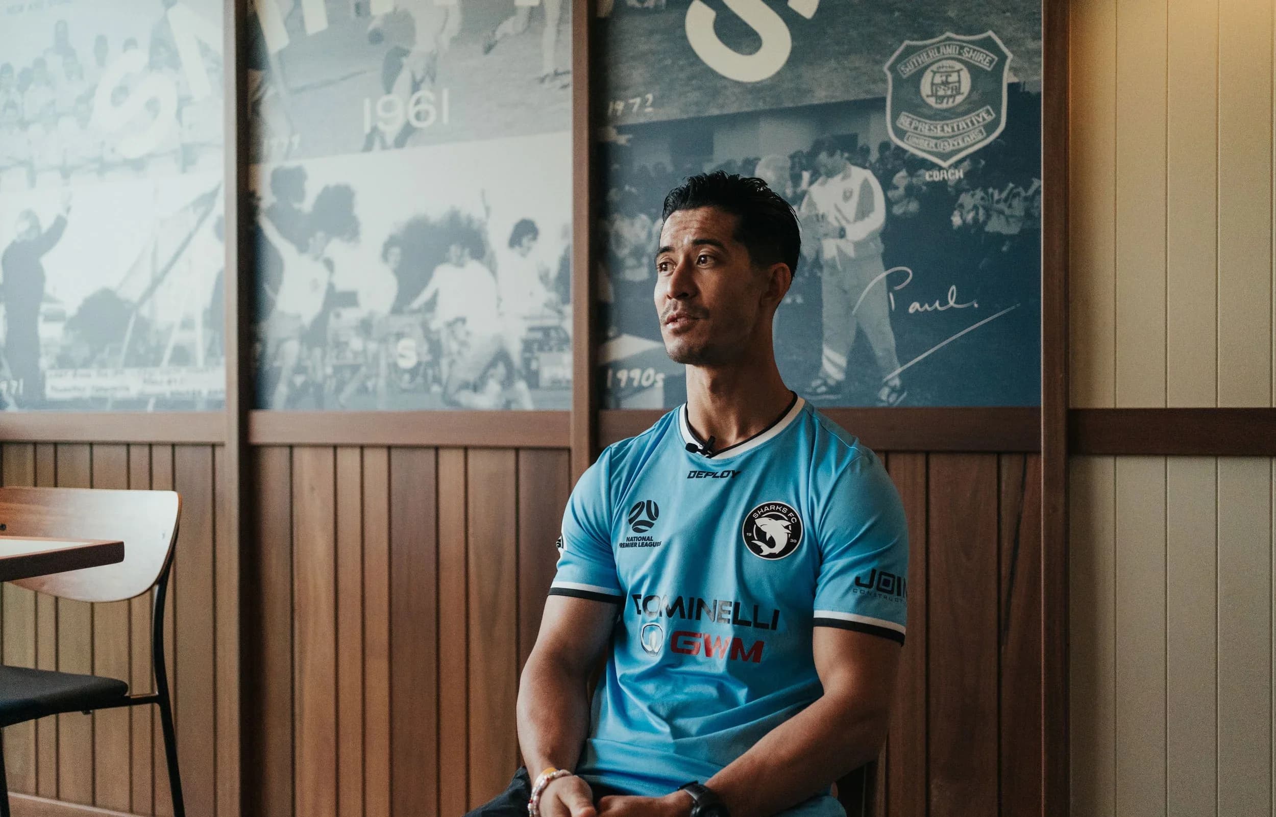 Brendan Gan sits in a sky-blue Sharks shirt in front of the club's historic photos