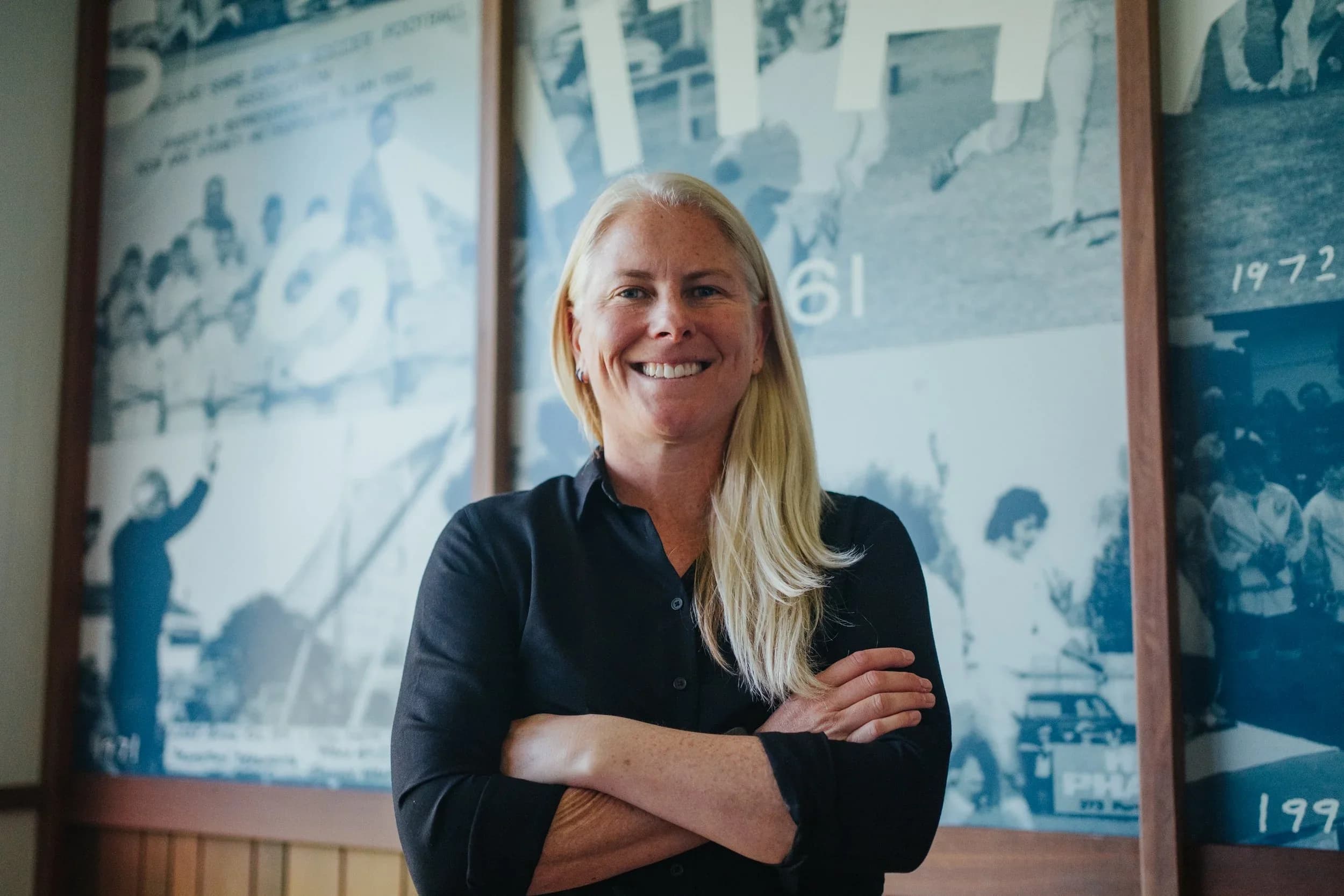 Alicia Ferguson, arms folded and smiling, in front of the club’s wall of historic photos