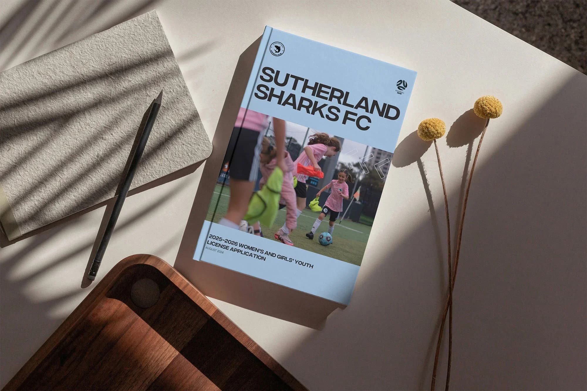 A Sutherland Sharks FC booklet on a desk beside flowers