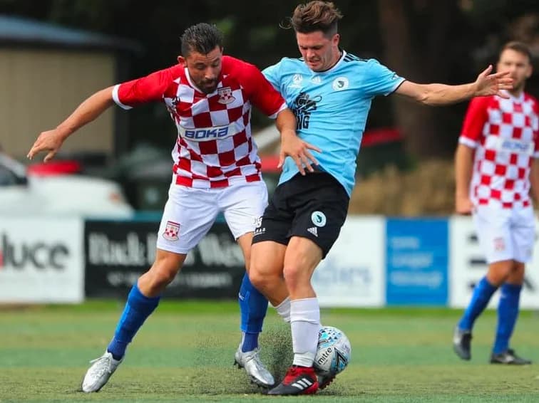 A Sharks player in sky blue tackles a Sydney United player in red and white