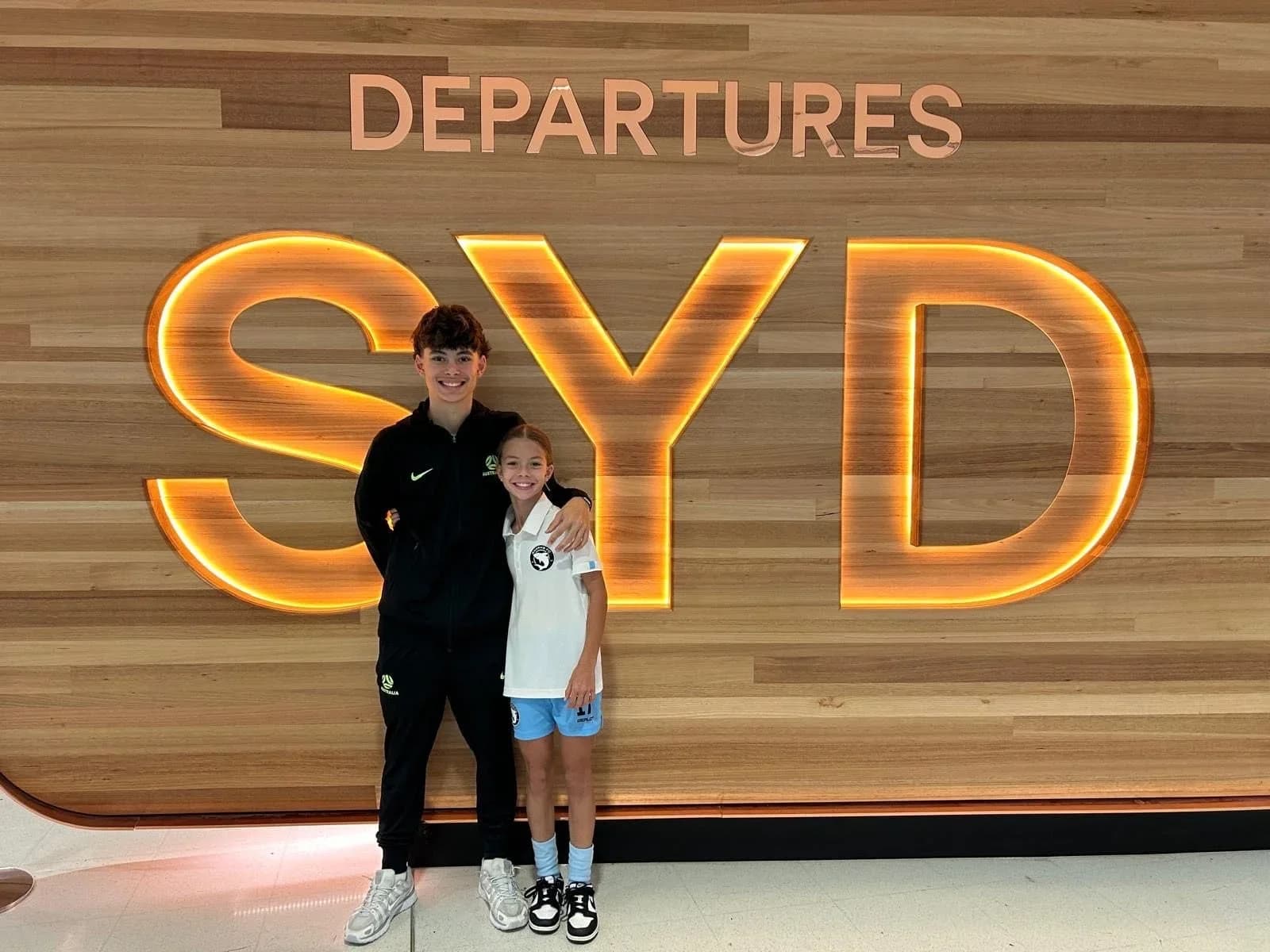Aston Reid and a family member in front of the Sydney Airport departures sign