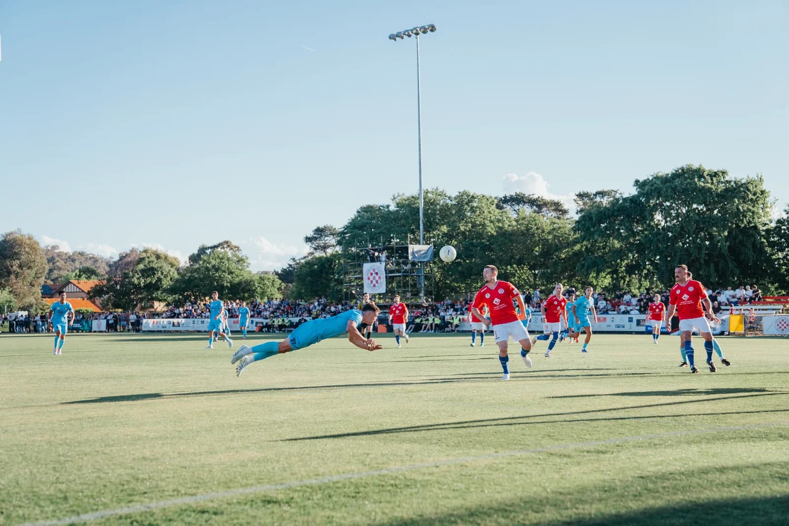 A Sharks player dives full length to head the ball as Canberra Croatia players look on