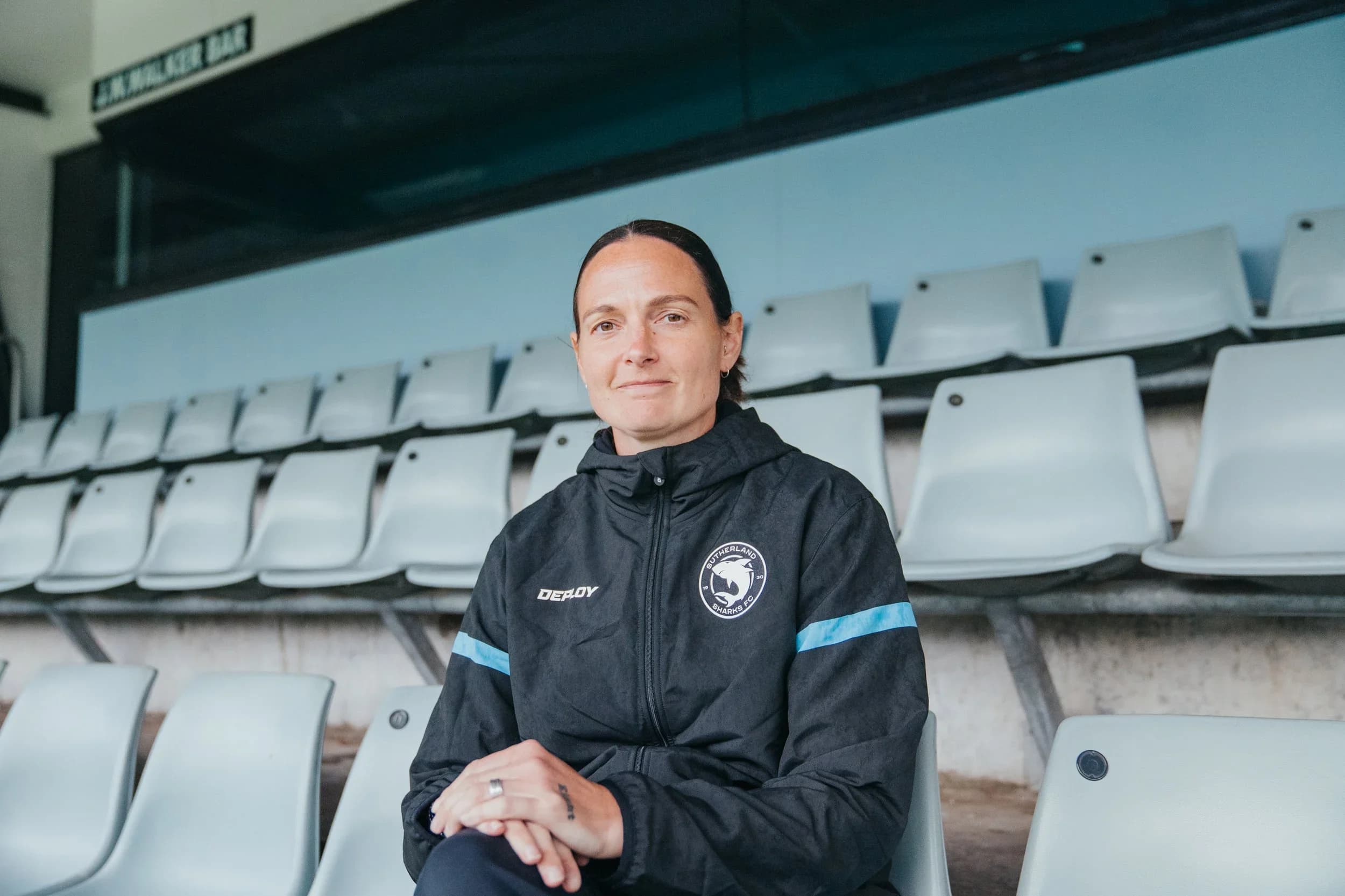 Charlotte Young in a Sharks jacket, seated in the empty stand at Seymour Shaw