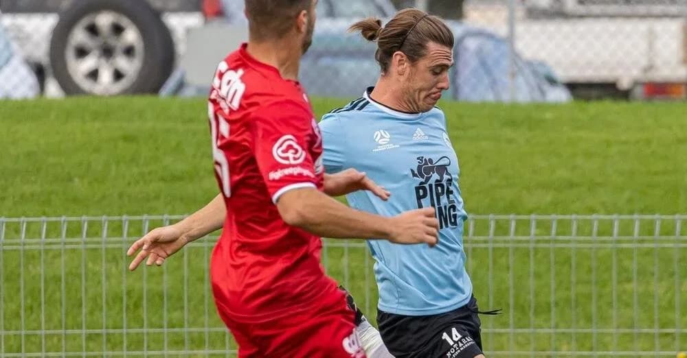 Chris Lindsay in sky blue battles an opponent in red for the ball