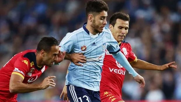 Chris Naumoff in sky blue on the ball between two opponents in red