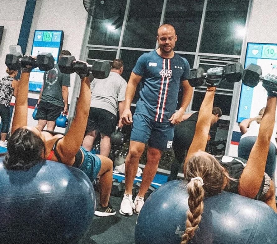 A trainer leads an F45 class lifting dumbbells on exercise balls