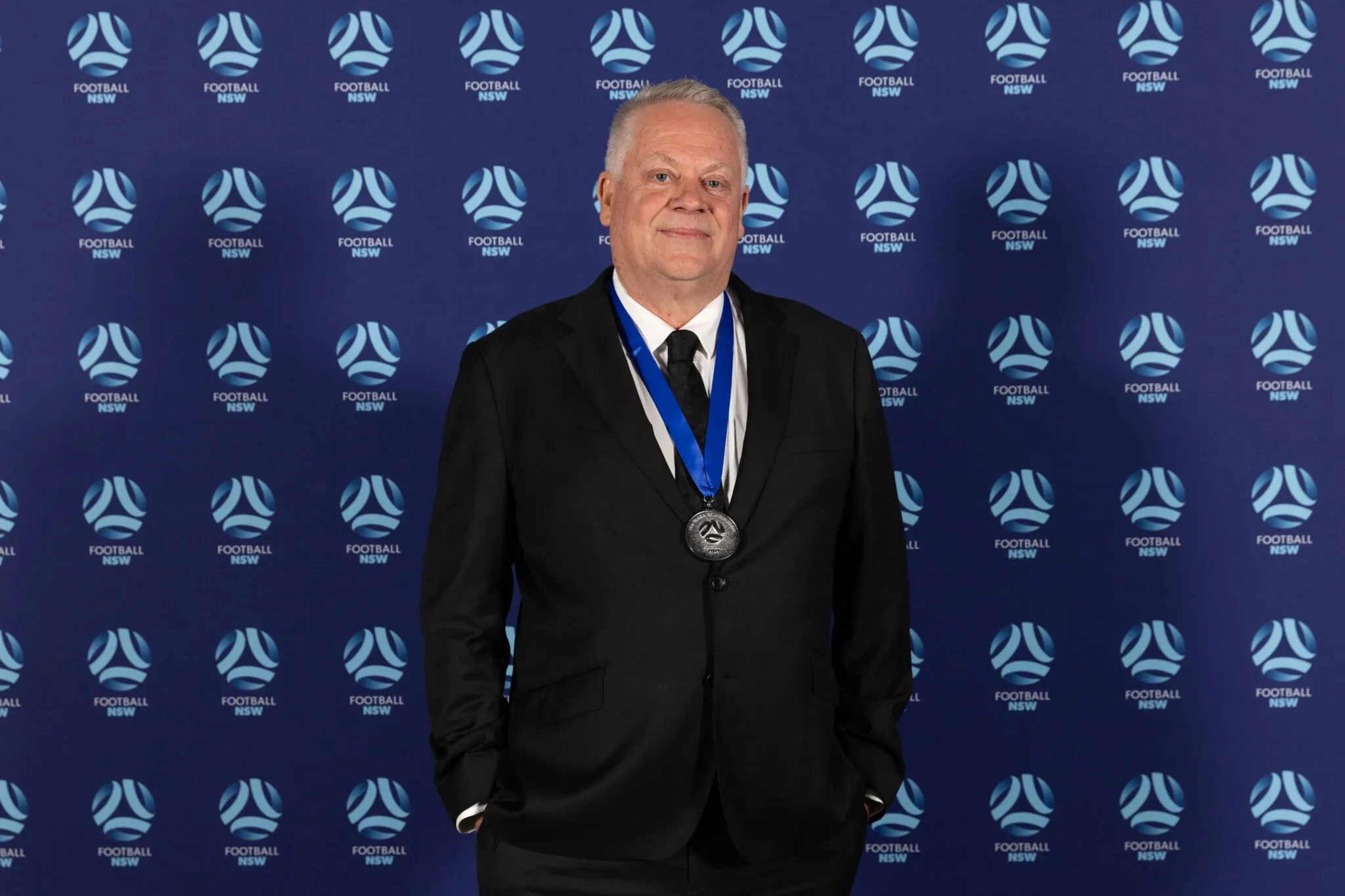 Greg O'Rourke wearing the Charles Valentine Medal in front of a Football Australia backdrop