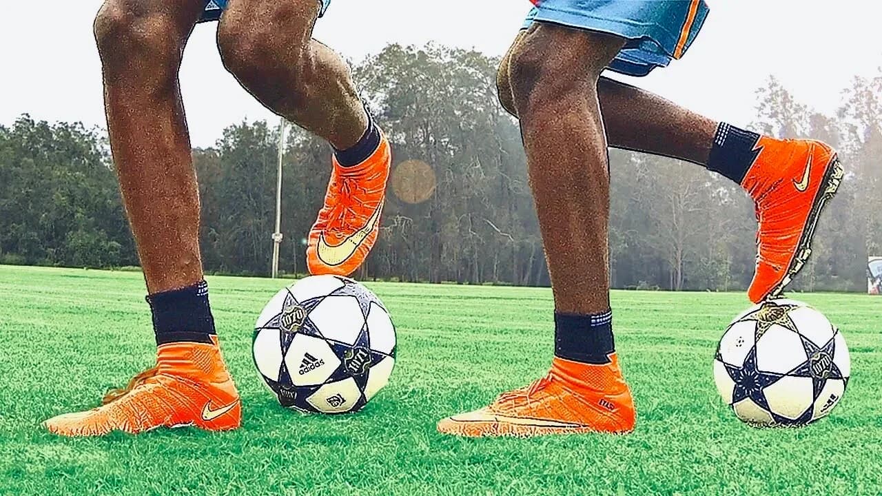 Two players' feet in orange boots on footballs