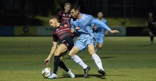 A Sharks player in sky blue battles a Wanderers player in red and black at night