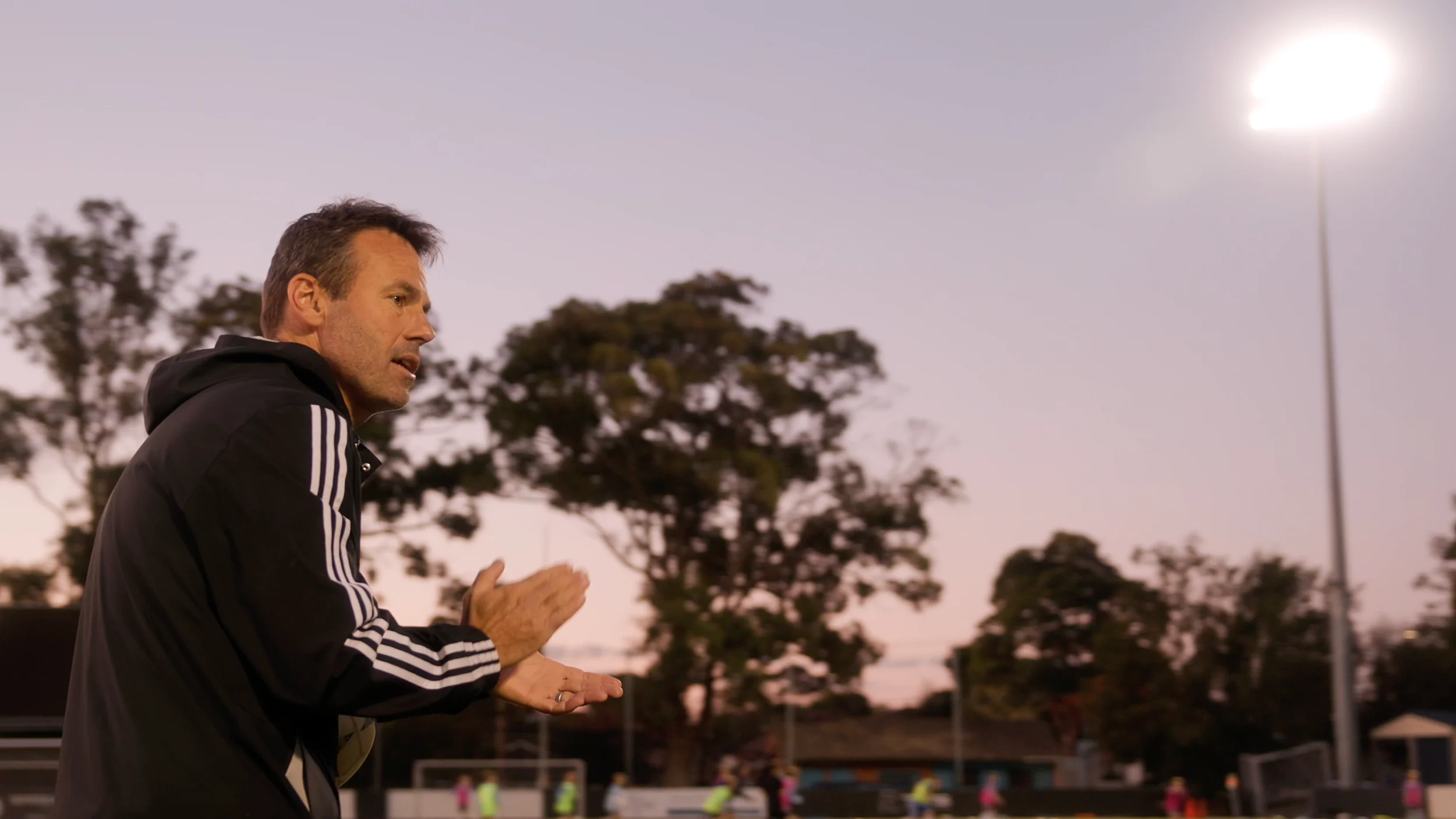 A Sharks coach claps on the sideline at dusk