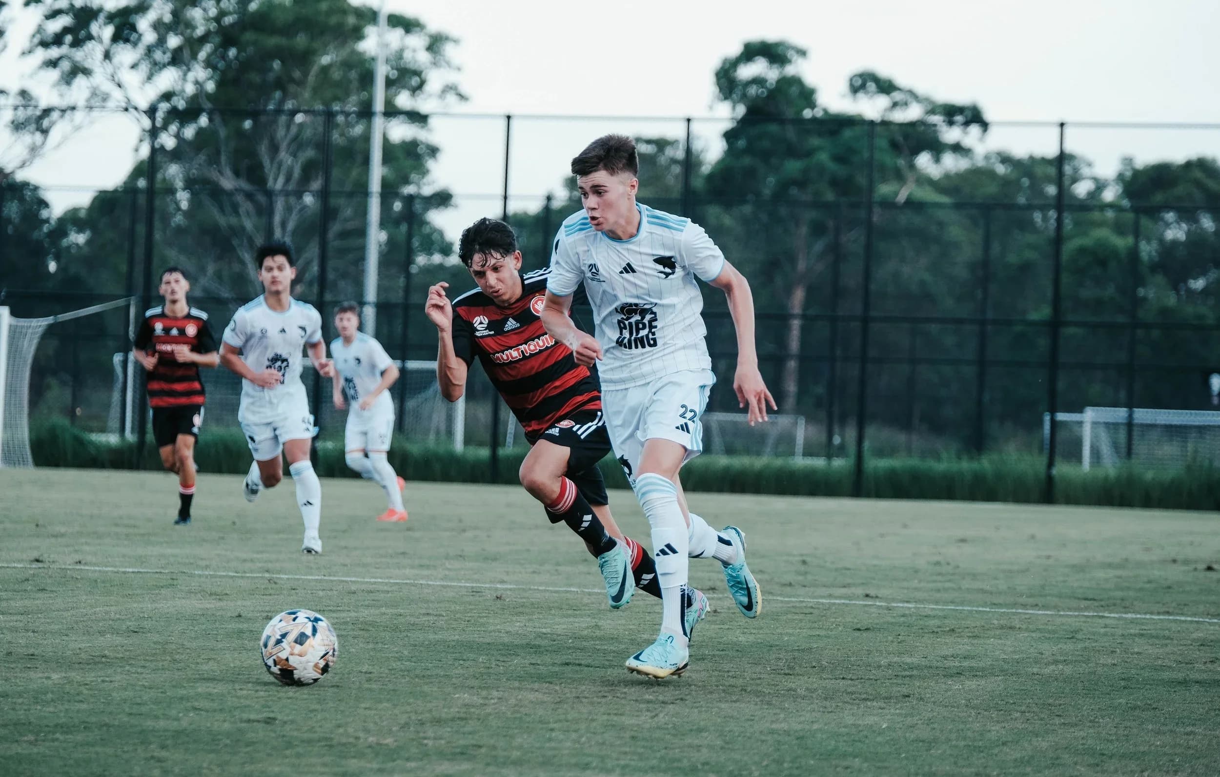 Jordan Graoroski in white runs with the ball against an opponent in red and black