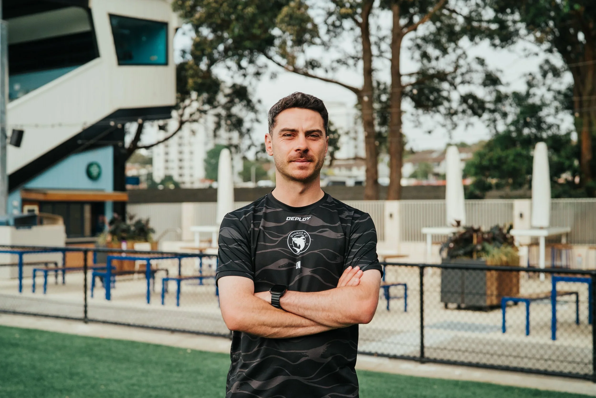 Kiki Naumoff, arms folded, in a black club training top outside the clubhouse