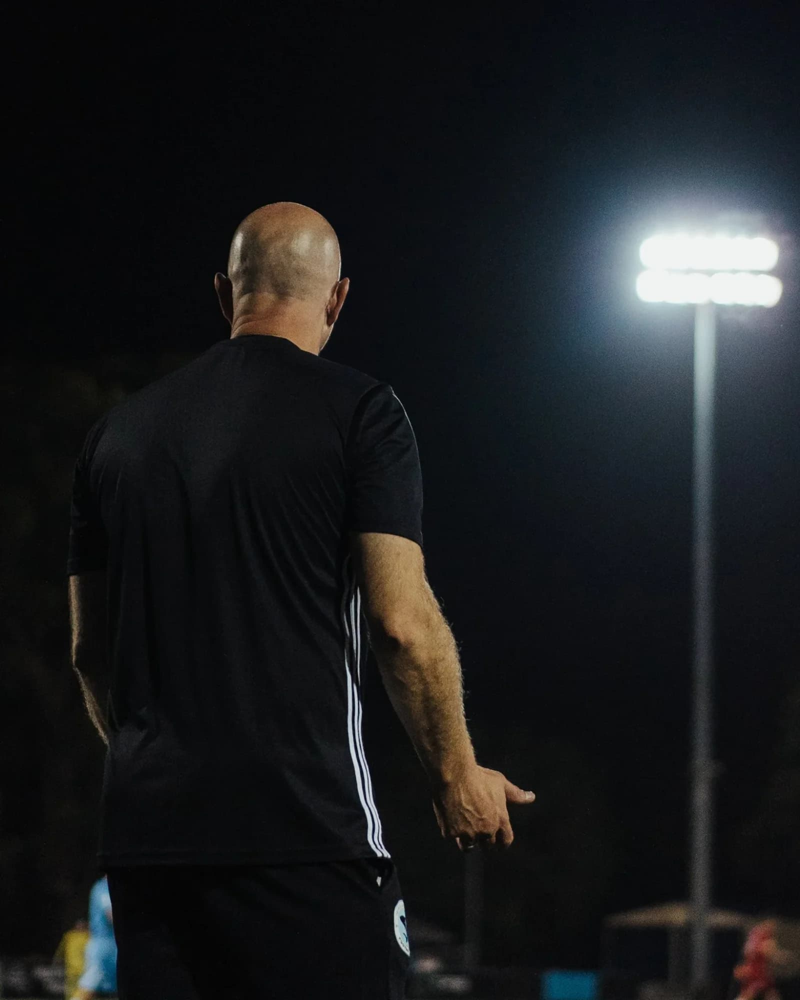 A coach in black watches from the sideline at night