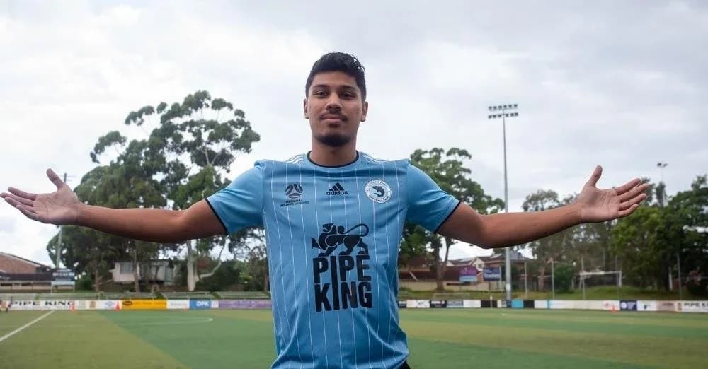 Madonis, arms outstretched, in a sky-blue Sharks shirt