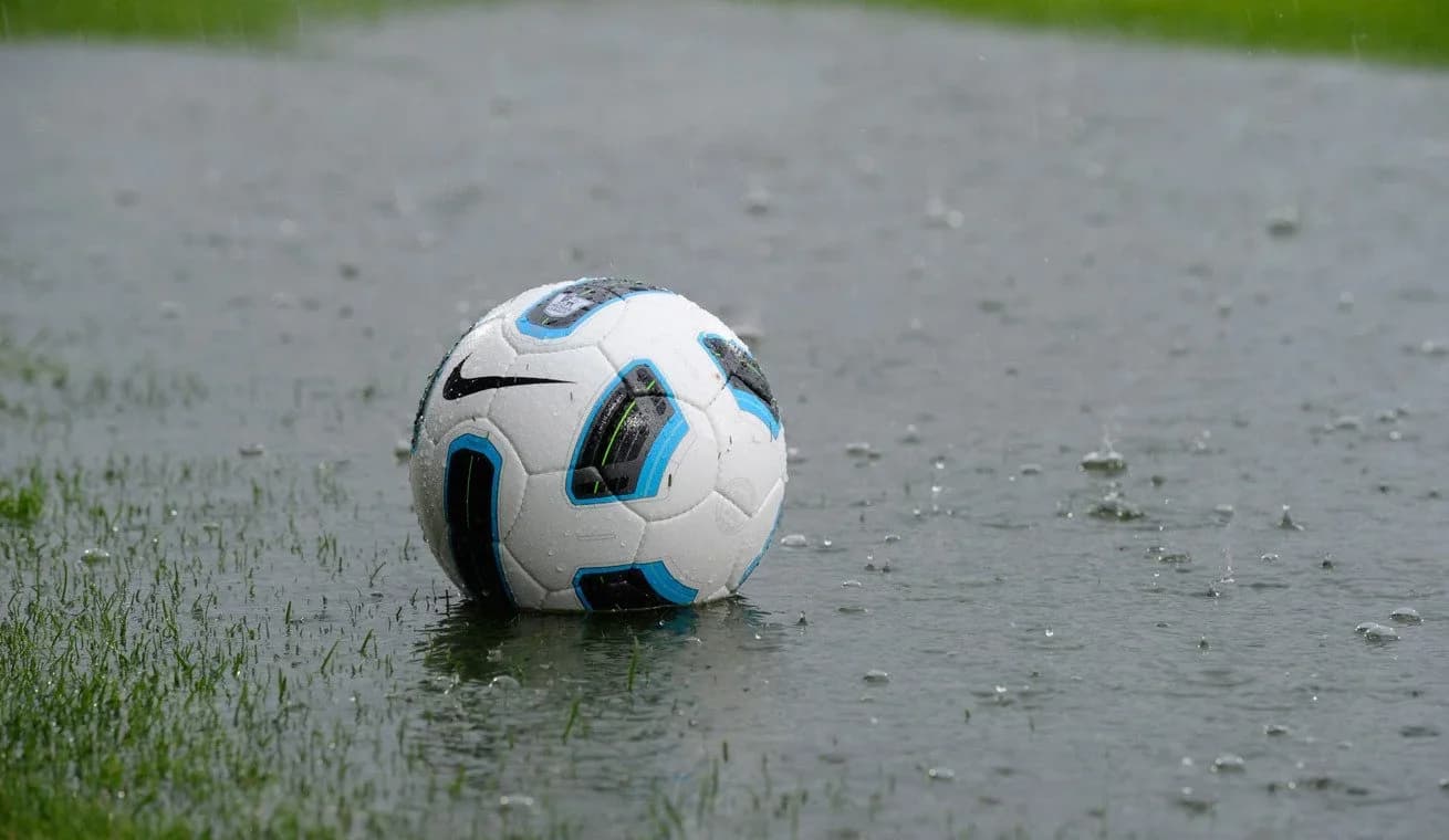 A football sits in a puddle on a waterlogged pitch