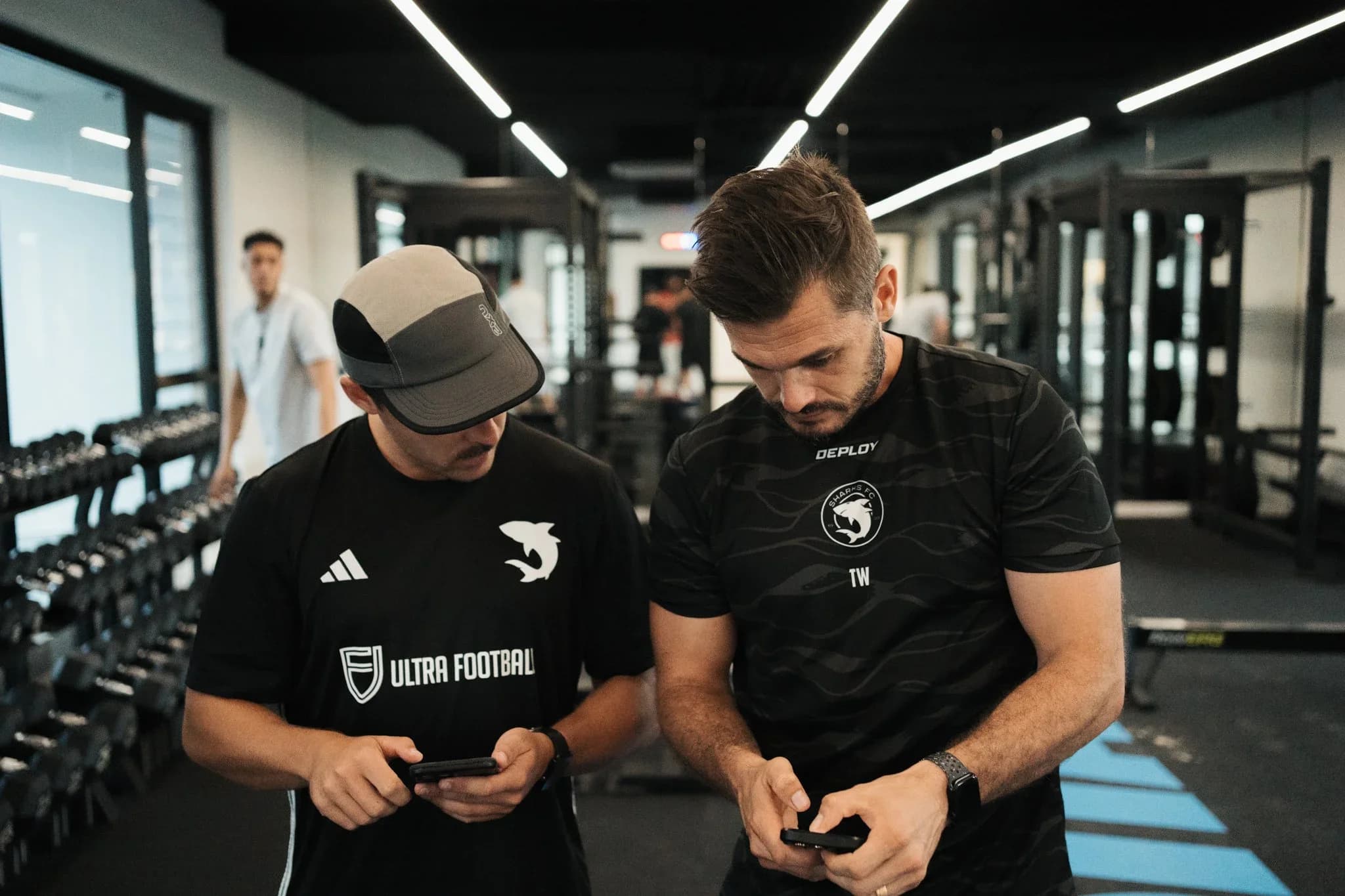 Two Sharks strength and conditioning coaches check a phone in the gym