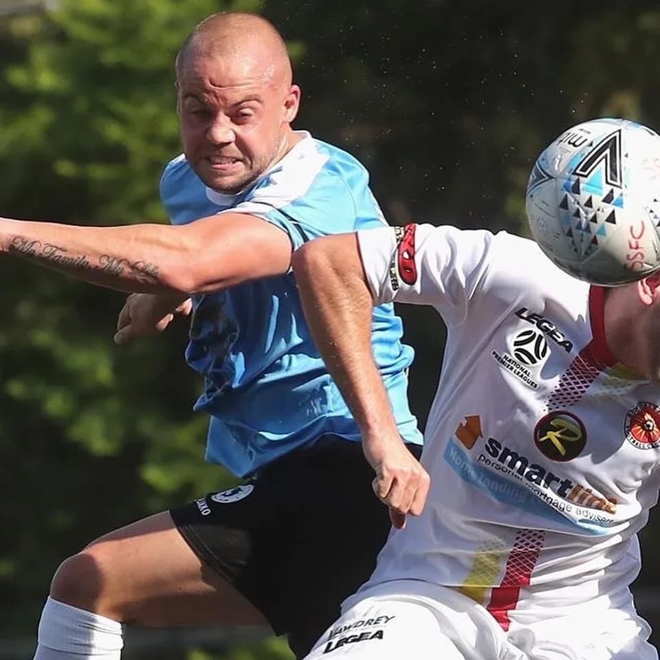 A Sharks player in sky blue rises for a header against an opponent in white