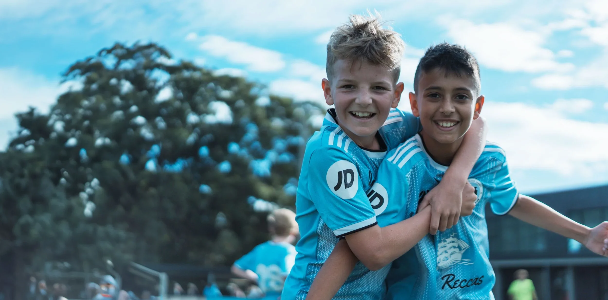 Two young players in sky-blue Sharks shirts hug and smile