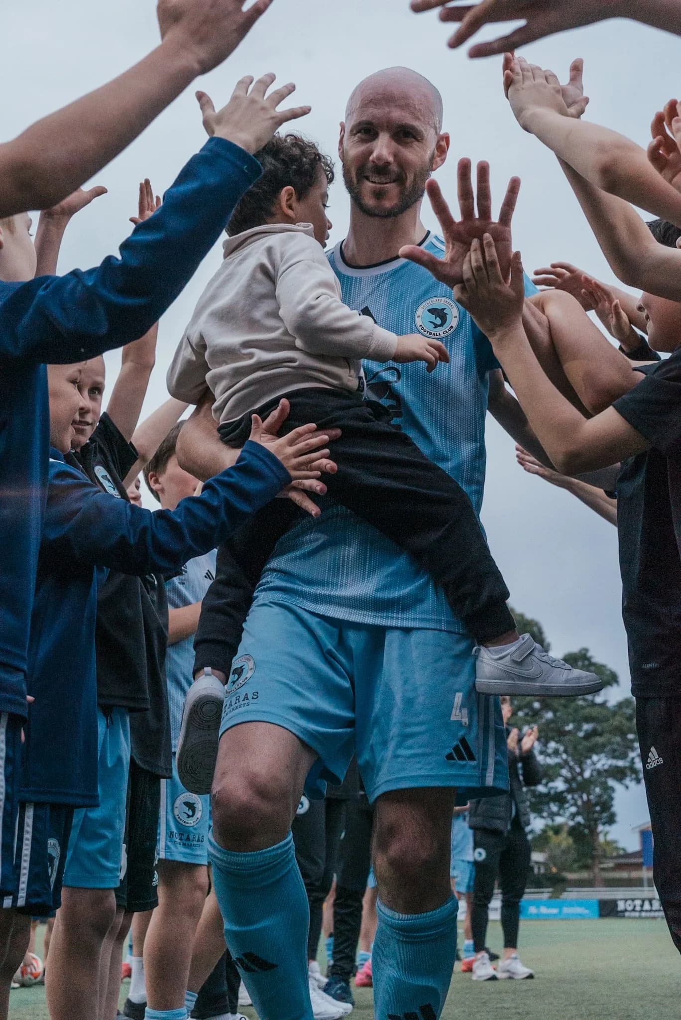 A Sharks player holds a young child as fans celebrate around him