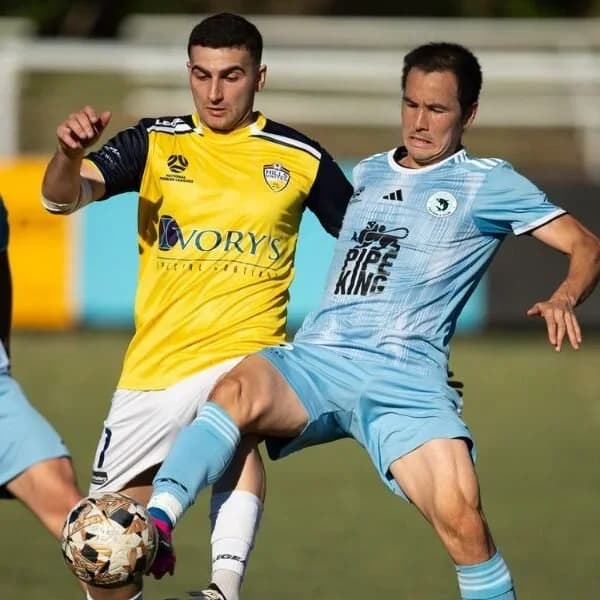 A Sharks player in sky blue battles for the ball with a Hills United player in yellow