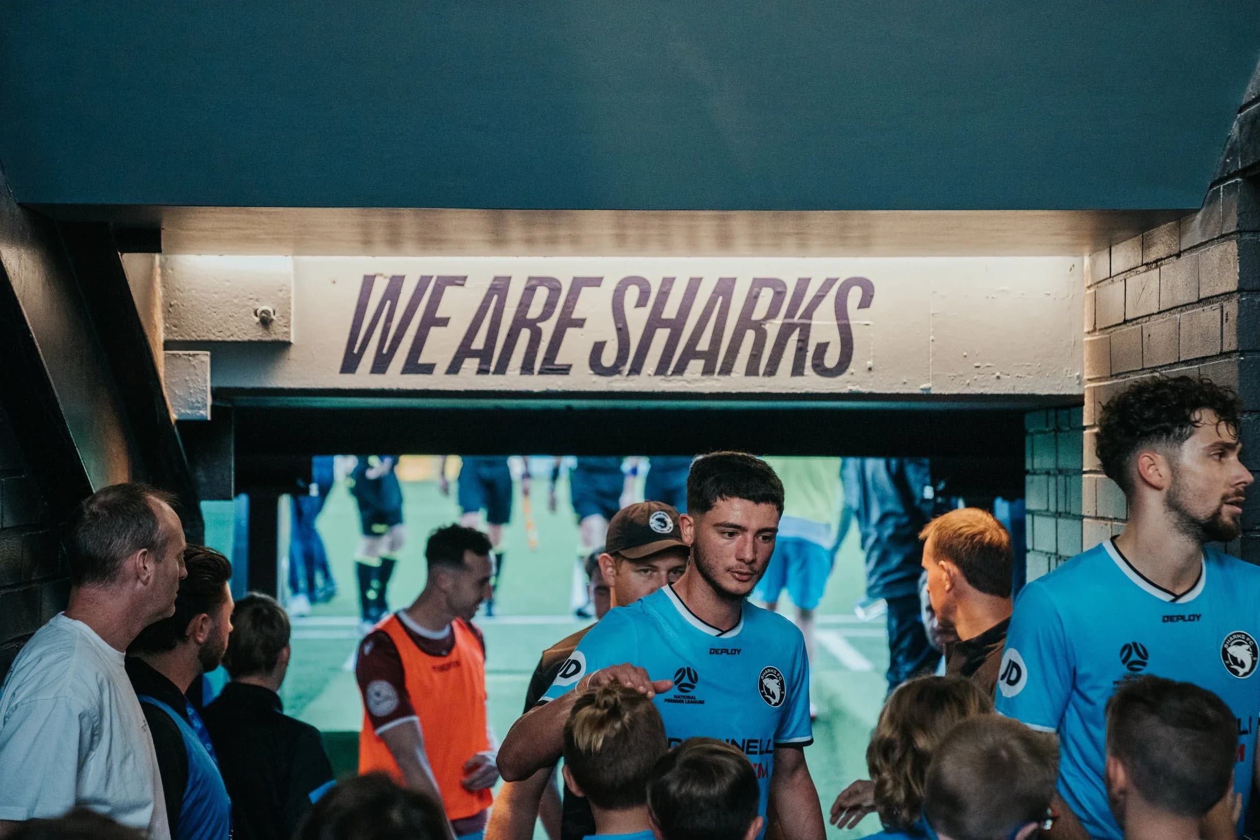 Sharks players walk through the tunnel past young fans under a We Are Sharks sign