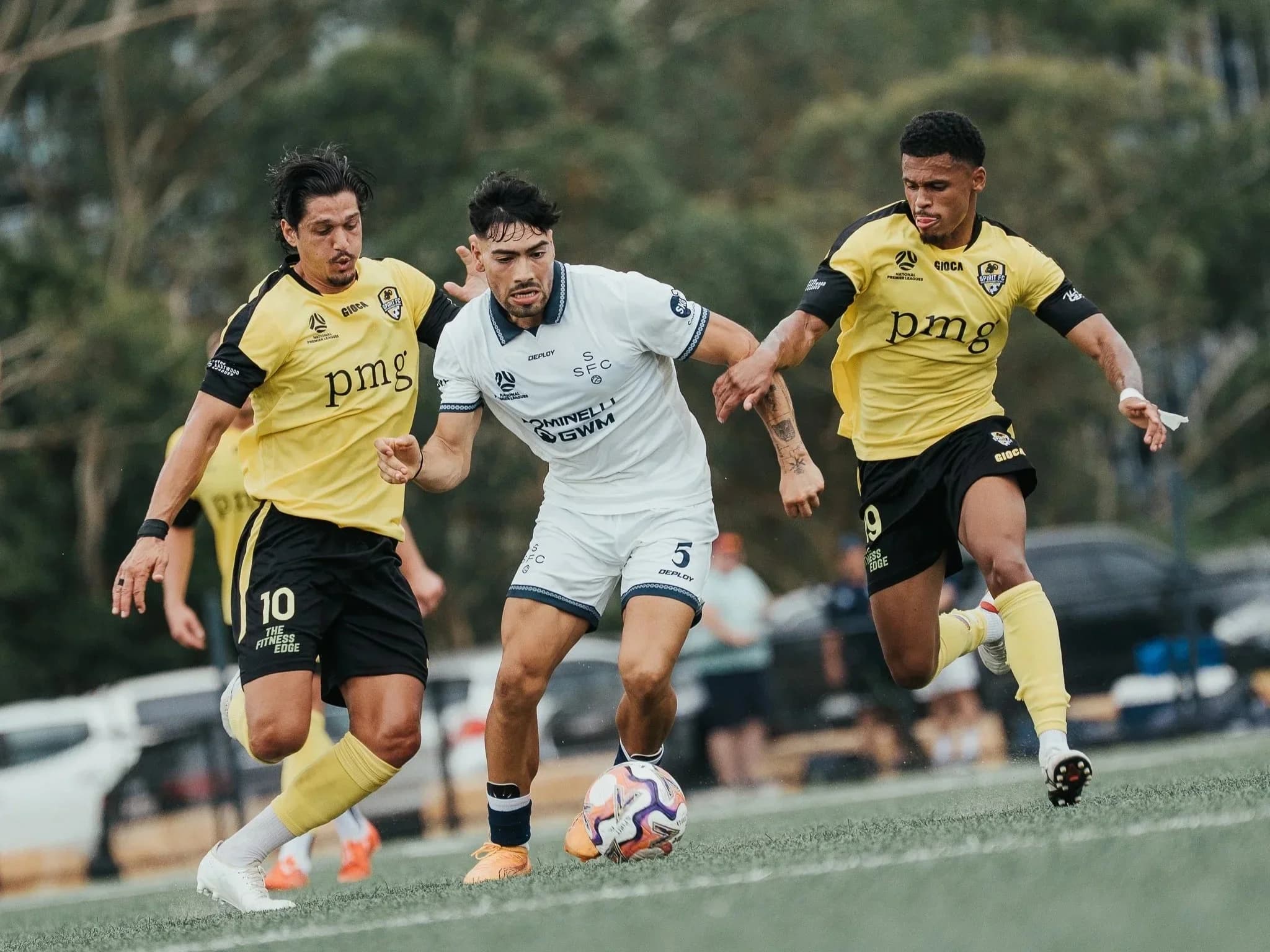 A Sharks player in white dribbles between two Spirit players in yellow at Christie Park