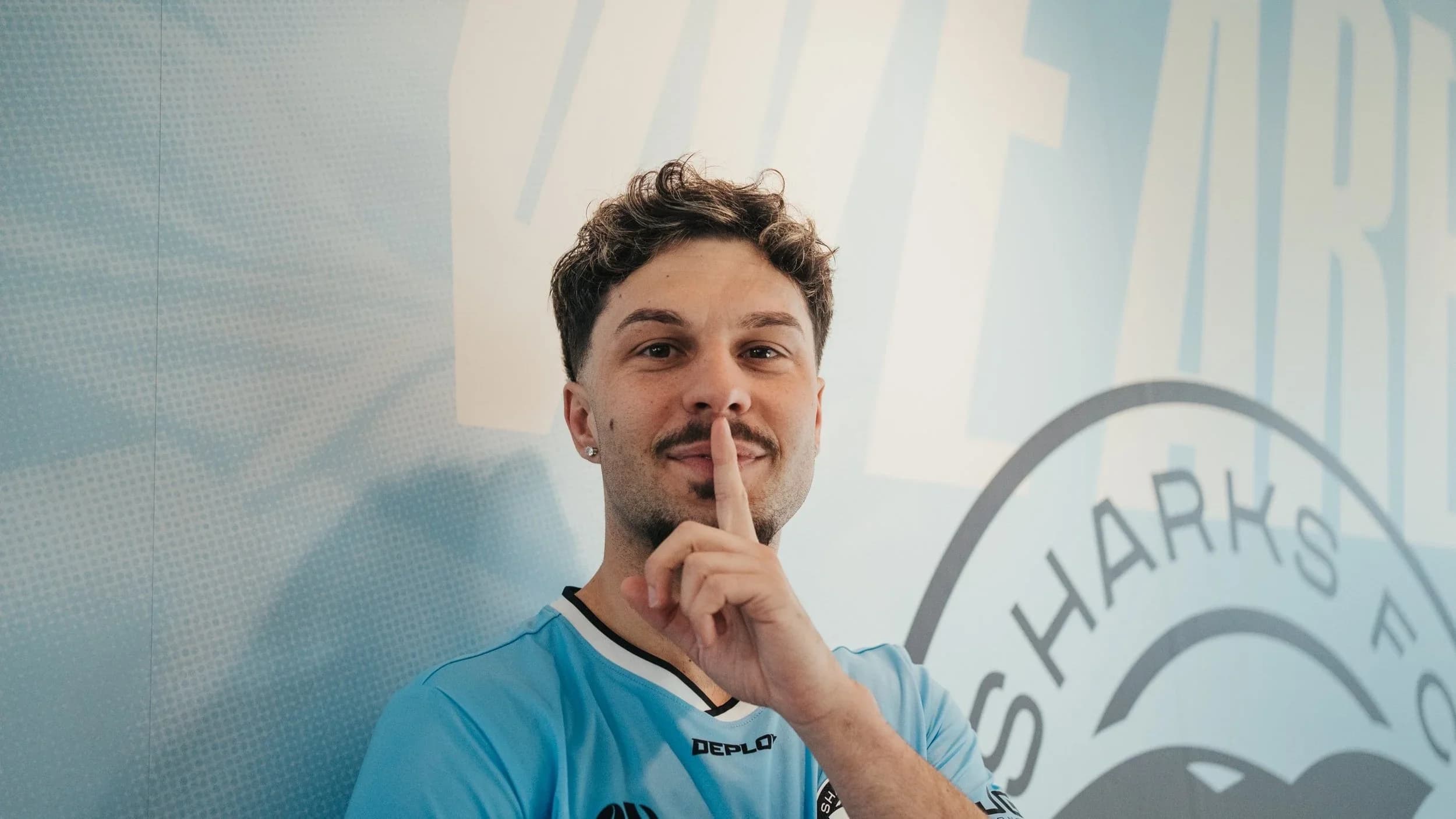 A Sharks player holds a finger to his lips in front of a large Sharks crest