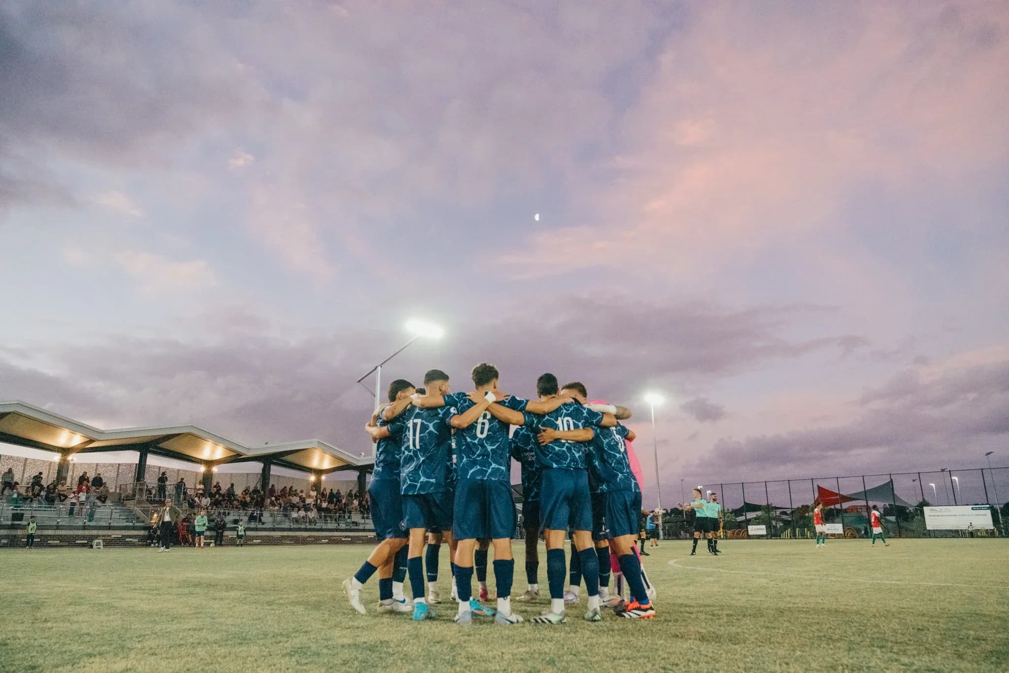 Sharks players huddle on the pitch under a pink sunset sky