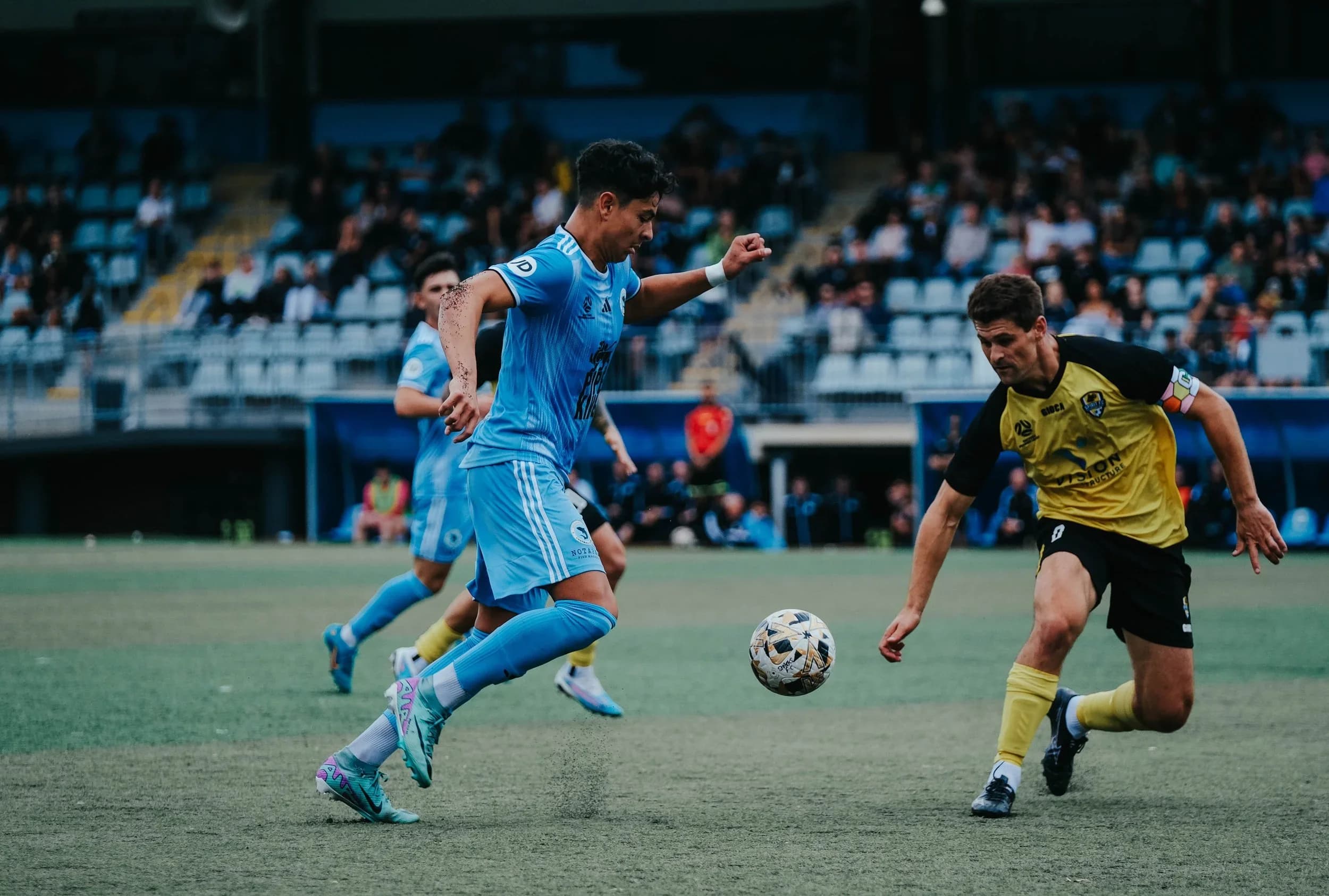 A Sharks player in sky blue runs with the ball against Spirit in yellow at Christie Park