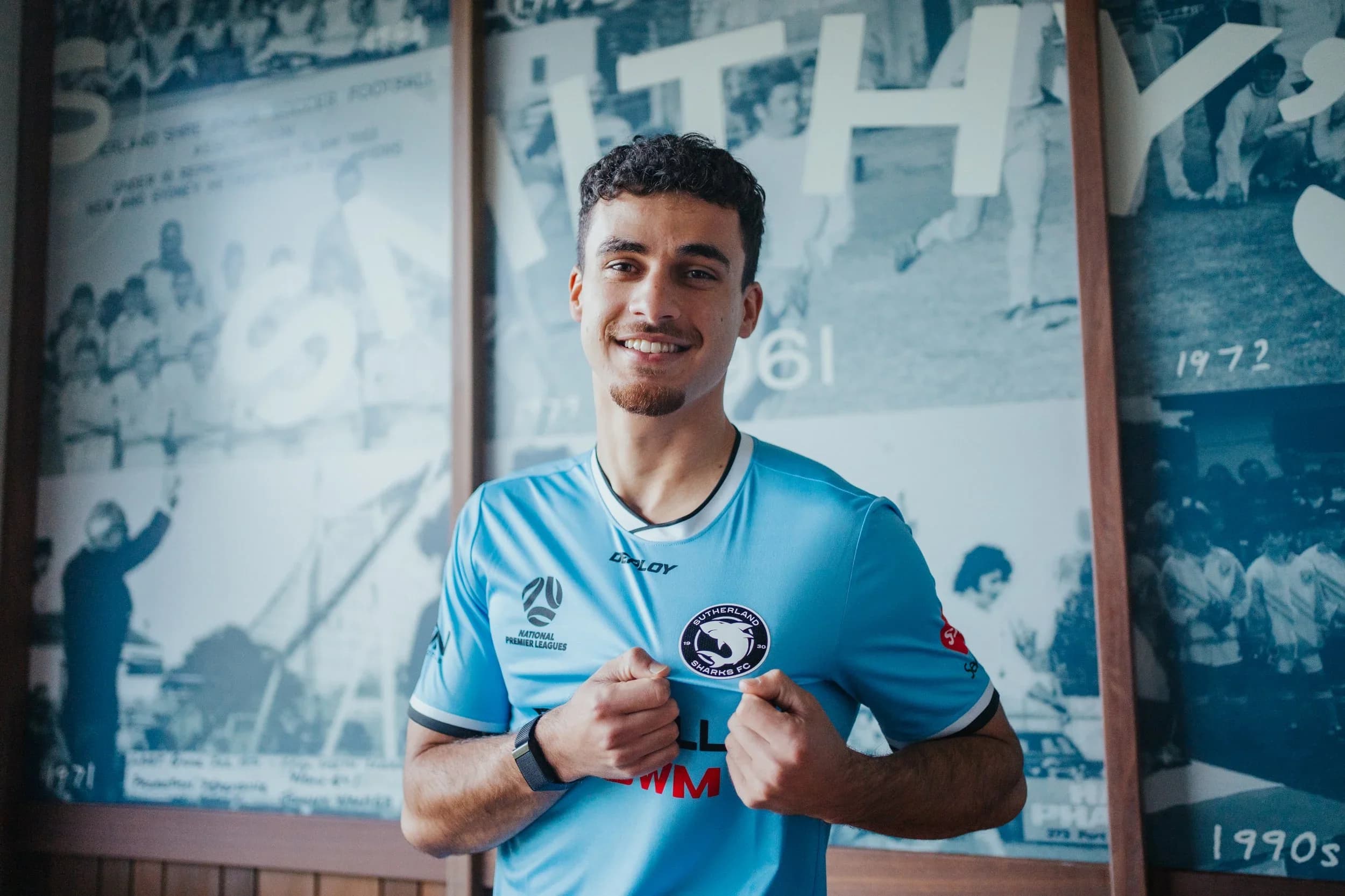 Diego Bonilla in a sky-blue Sharks shirt, smiling in front of the club's historic photos