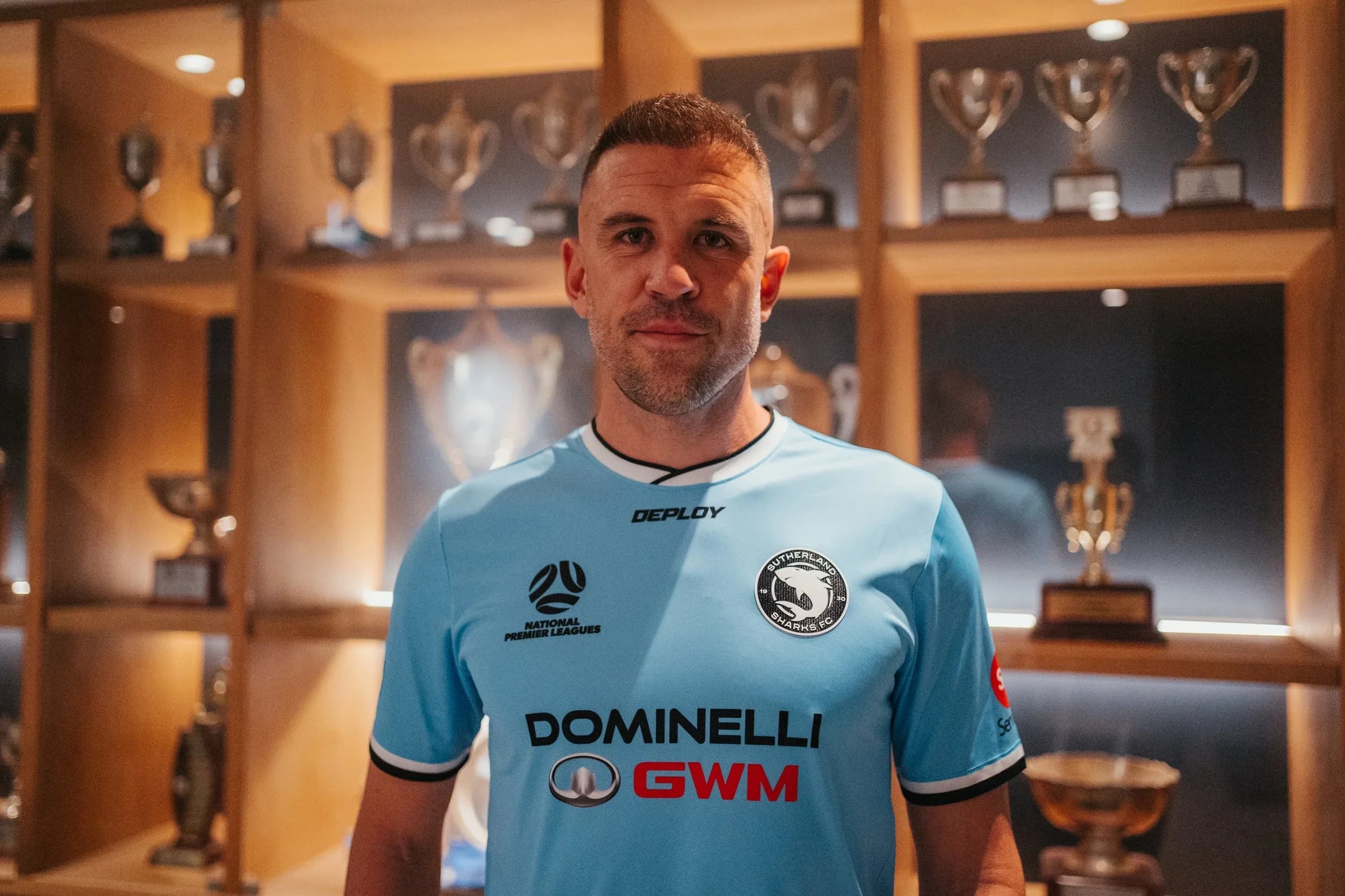 Matthew Jurman in a sky-blue Sharks shirt in front of the club's trophy cabinet