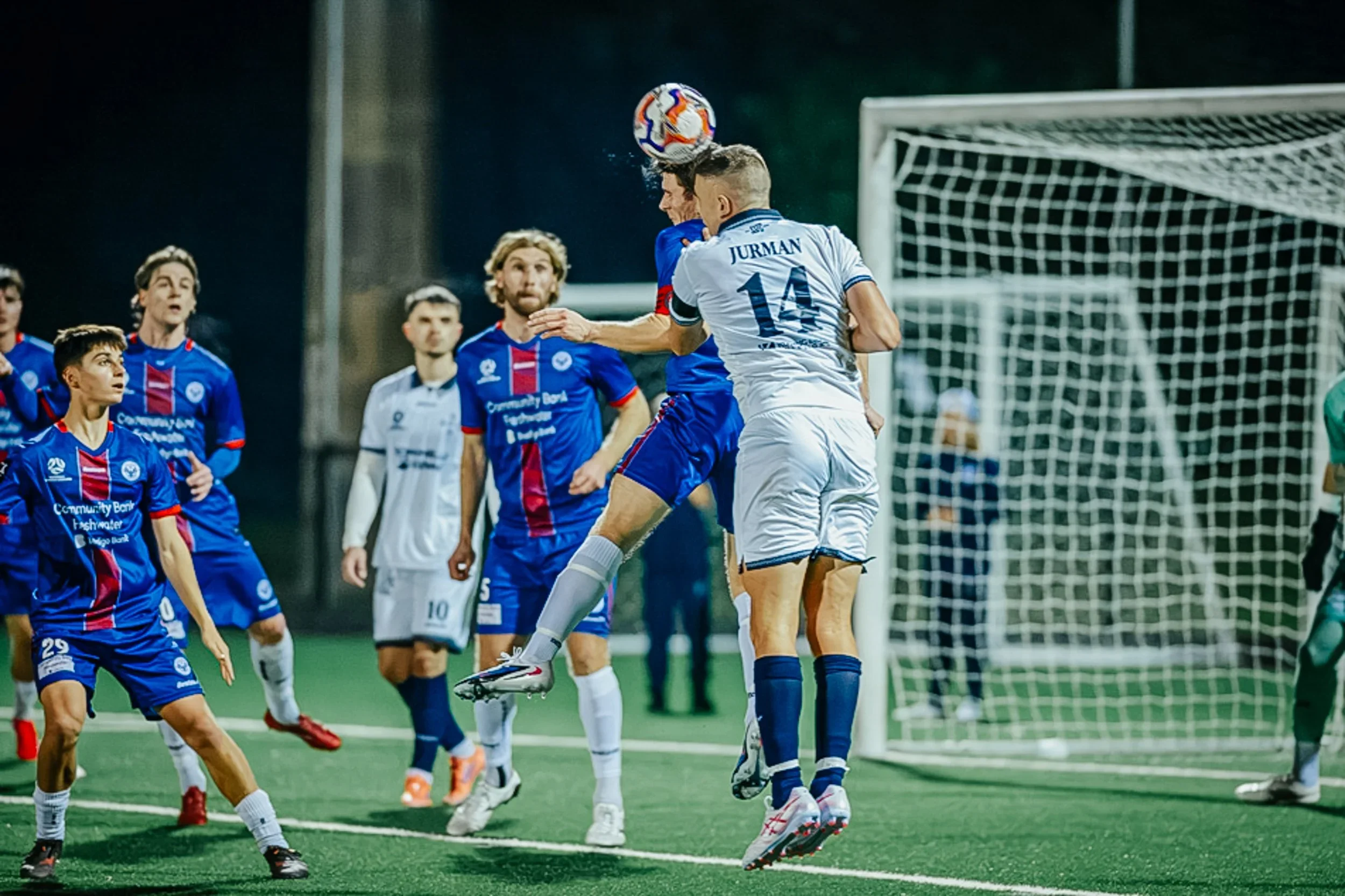 A Sharks player in white rises to head the ball in a crowded goalmouth