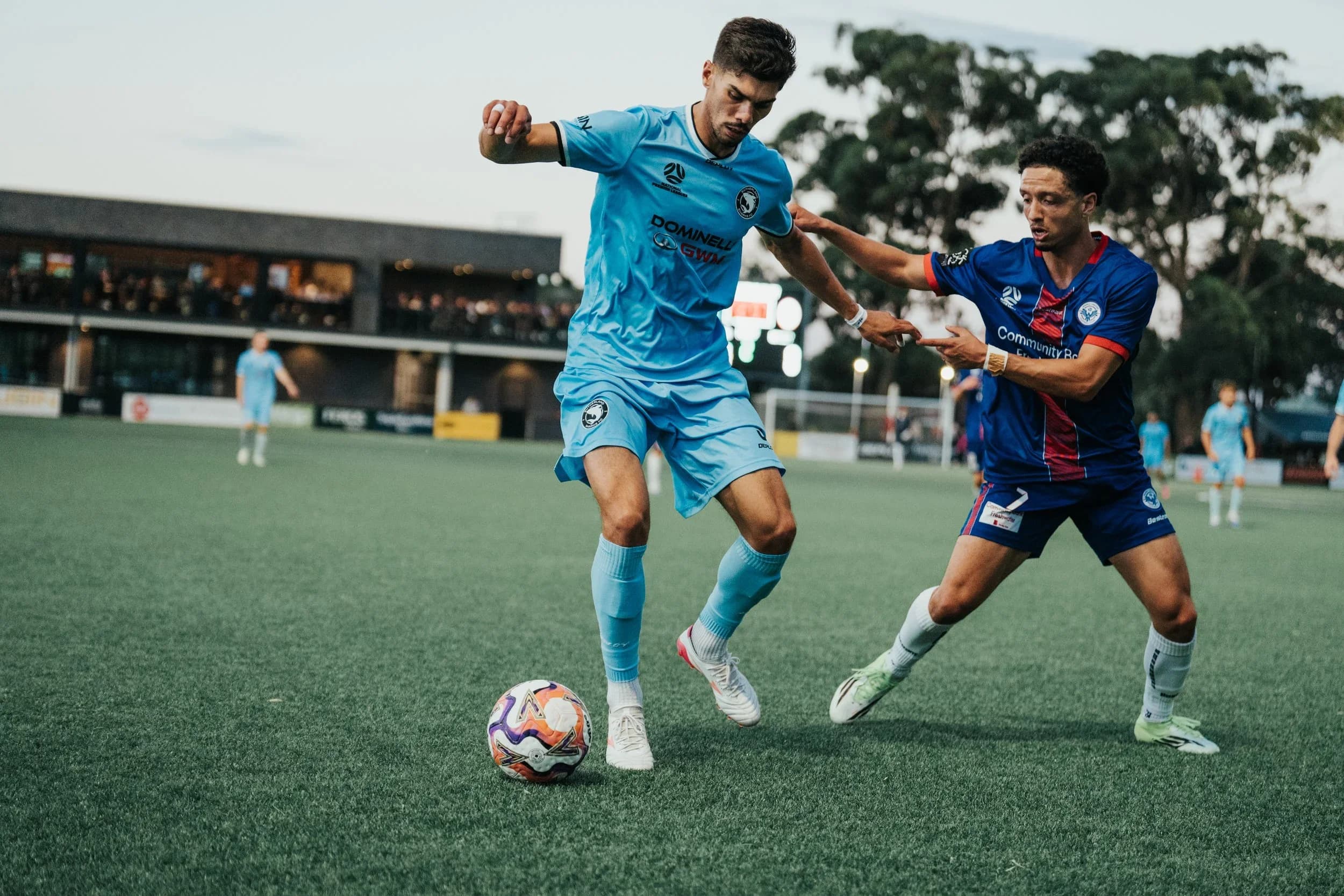 A Sharks player in sky blue and an opponent in blue and red battle for the ball