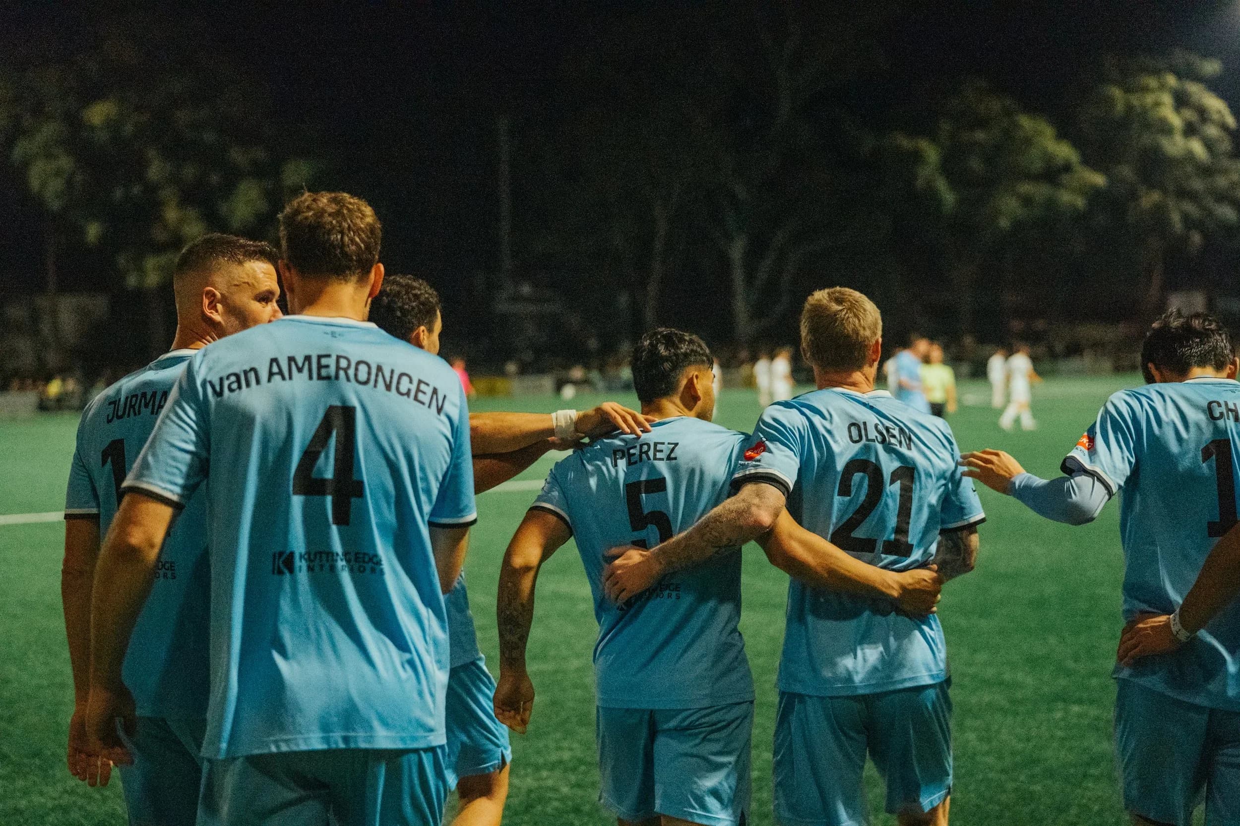 Sharks players huddle together on the pitch at night