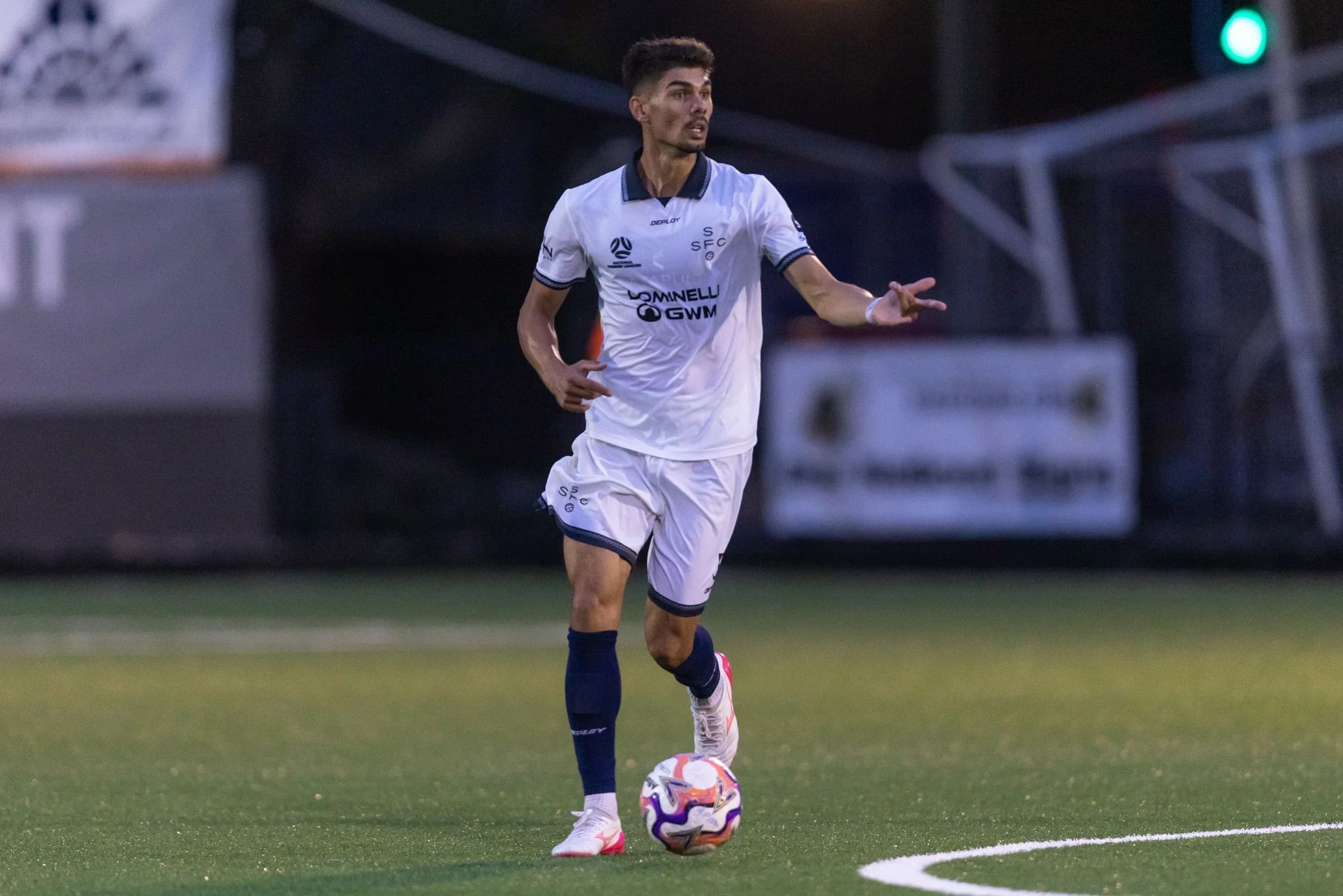 A Sharks player in white runs with the ball against Olympic at night