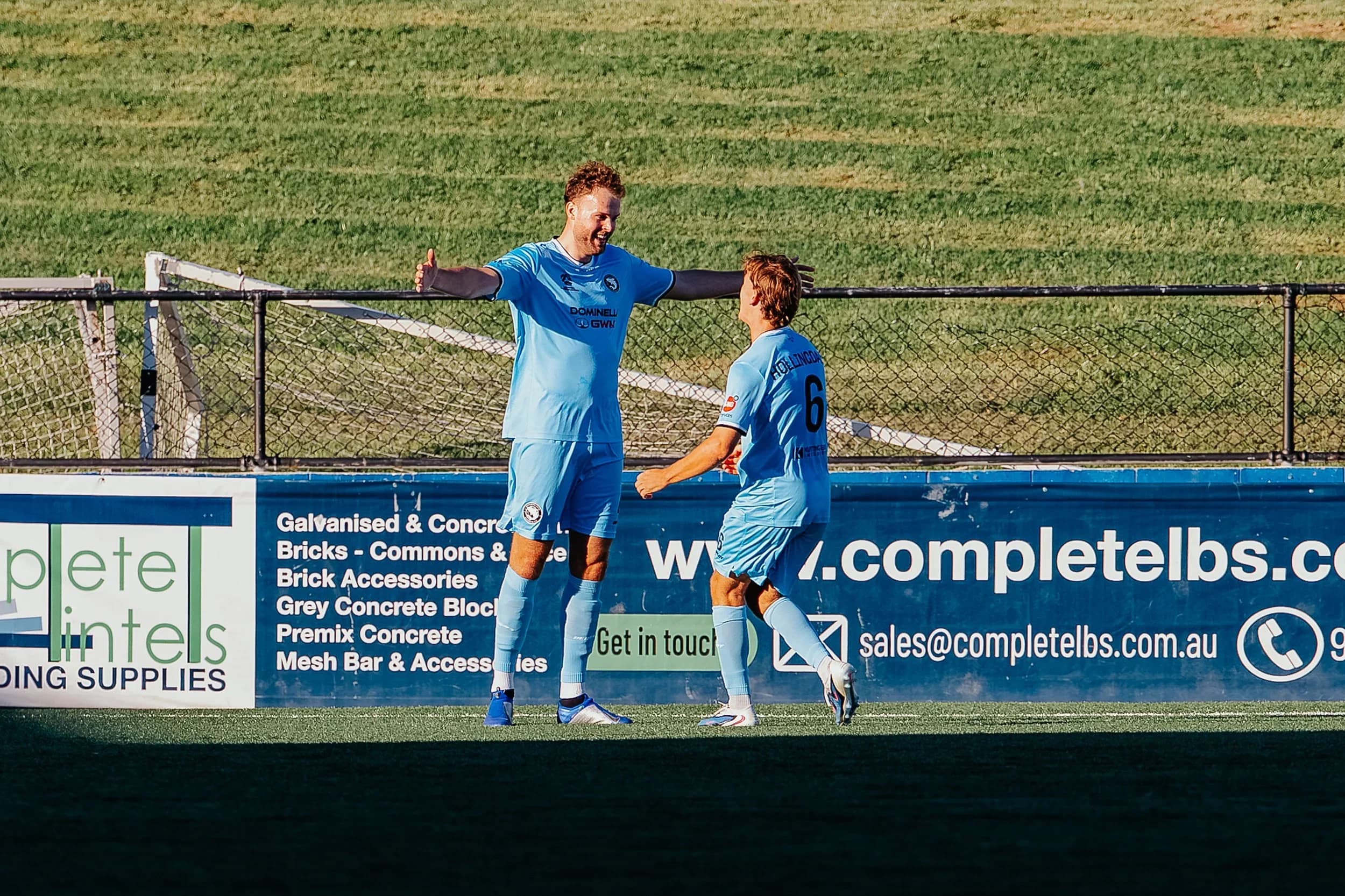Sharks players celebrate a goal in front of the advertising boards at Sydney United