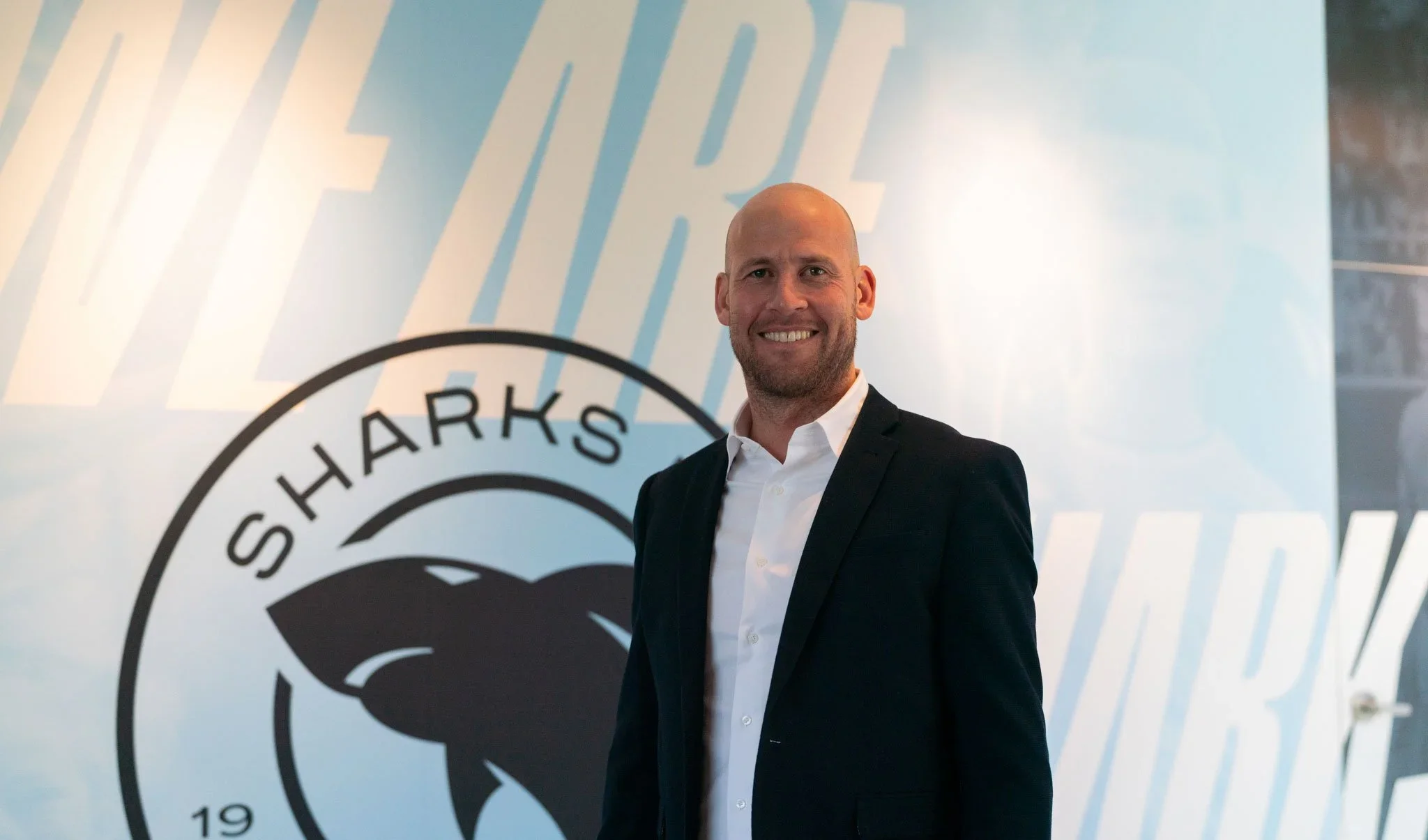 Trent McClenahan smiling in front of a large Sharks crest