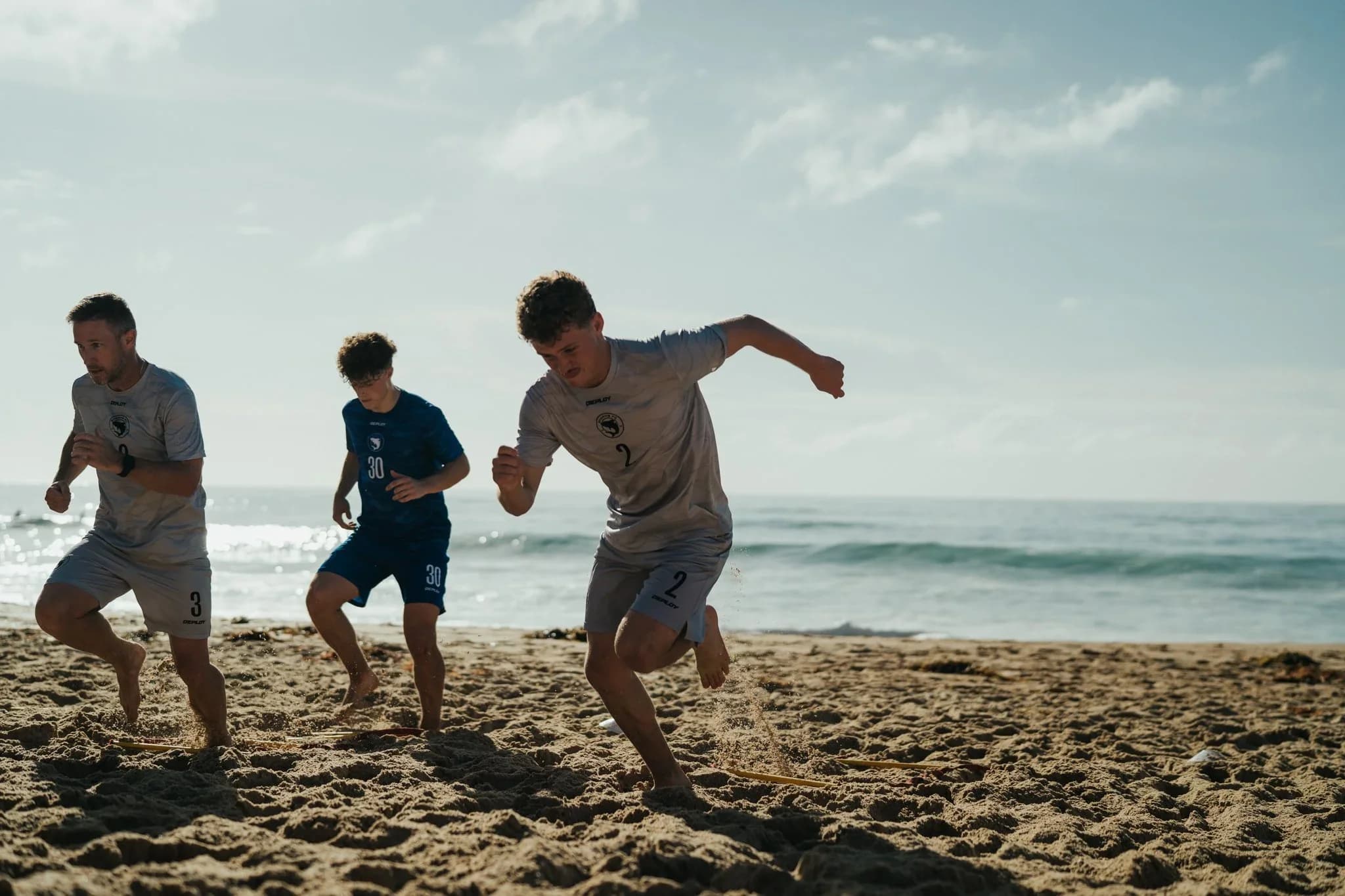 Three young men play football on a Sutherland Shire beach