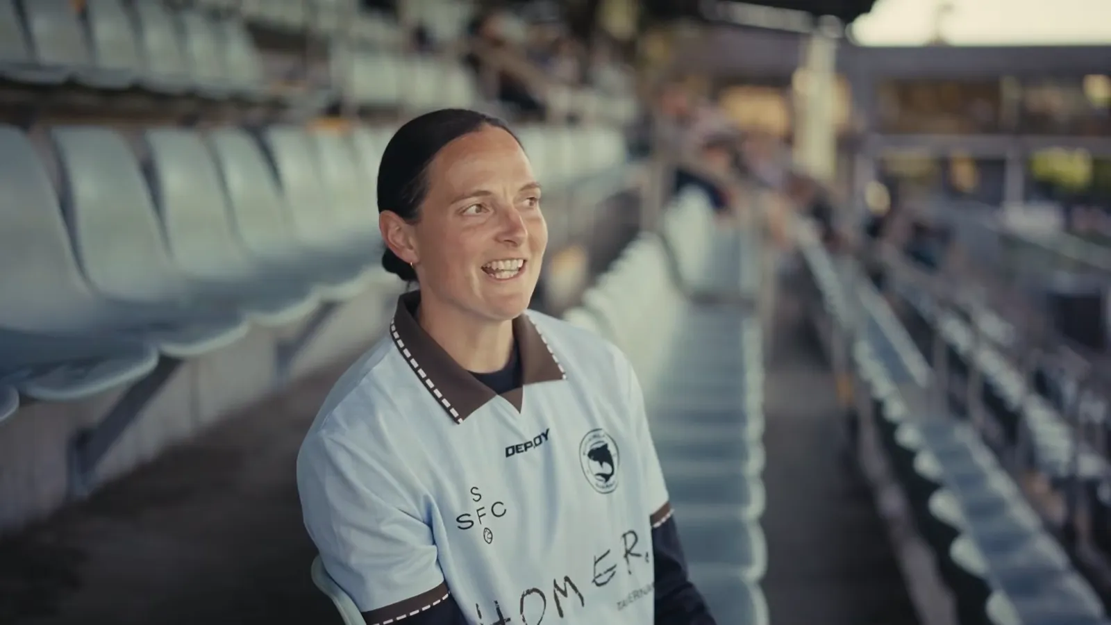 Charlotte Young, the Girls Youth Technical Director, smiling in a Sharks shirt in the empty stand at Seymour Shaw